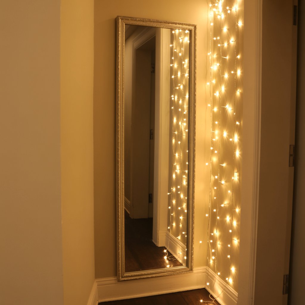 Tall narrow mirror in hallway reflecting string lights
